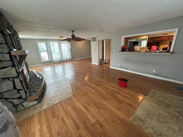 unfurnished living room with ceiling fan, a stone fireplace, a textured ceiling, and hardwood / wood-style flooring