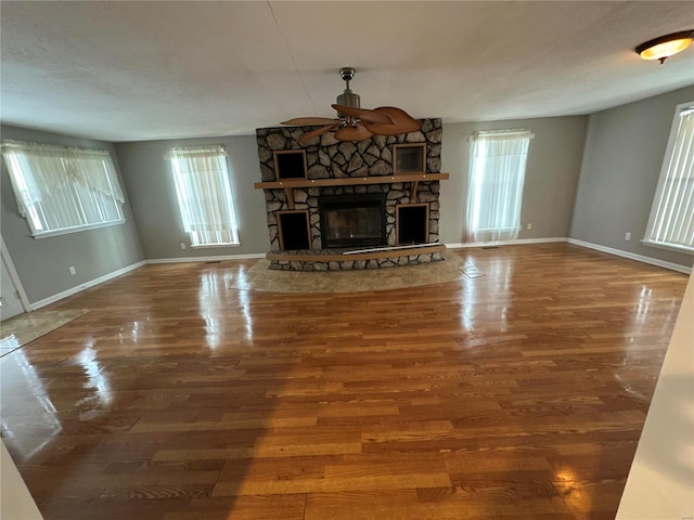 unfurnished living room featuring ceiling fan, hardwood / wood-style floors, and a stone fireplace