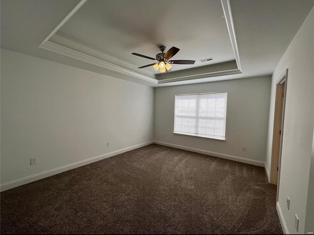 empty room with ceiling fan, dark carpet, and a tray ceiling