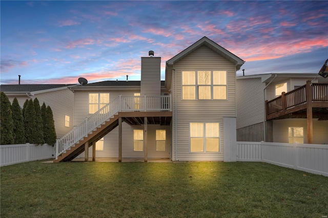 back house at dusk featuring a wooden deck and a yard