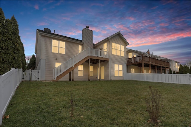 back house at dusk featuring a wooden deck and a lawn