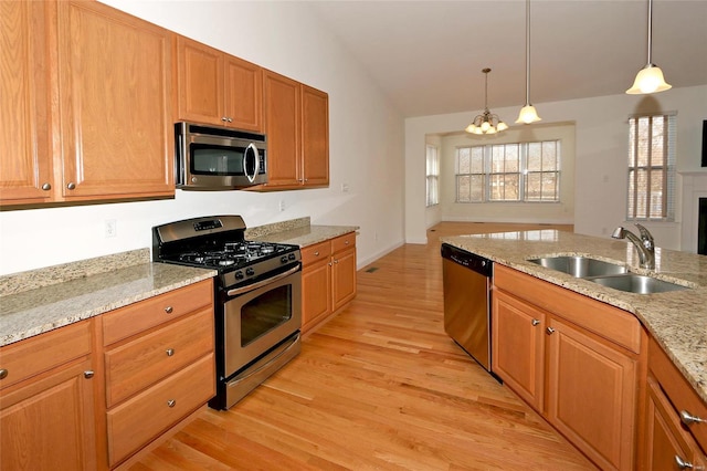 kitchen featuring sink, appliances with stainless steel finishes, light stone counters, decorative light fixtures, and vaulted ceiling