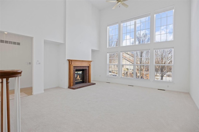 unfurnished living room featuring carpet floors, a towering ceiling, visible vents, a ceiling fan, and a brick fireplace