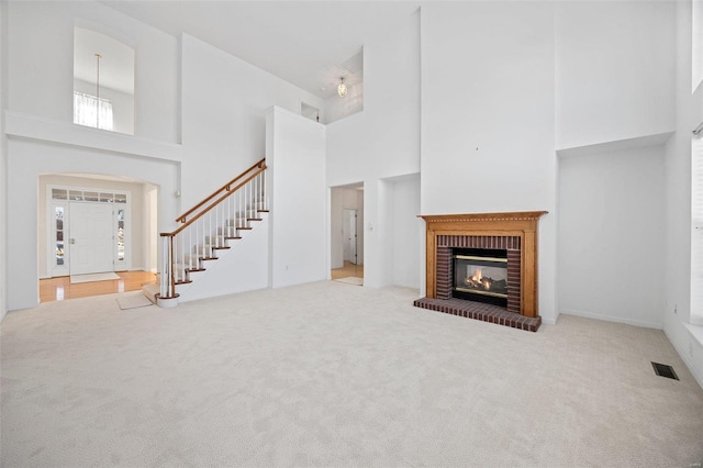 unfurnished living room with visible vents, a towering ceiling, carpet, stairs, and a brick fireplace