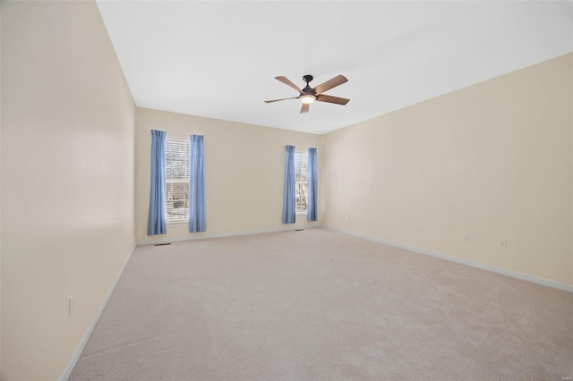 spare room with a ceiling fan, light colored carpet, and baseboards