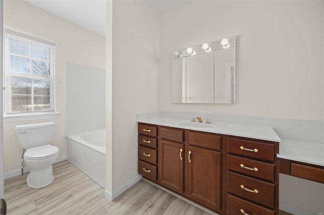 bathroom featuring a tub to relax in, baseboards, toilet, wood finished floors, and vanity