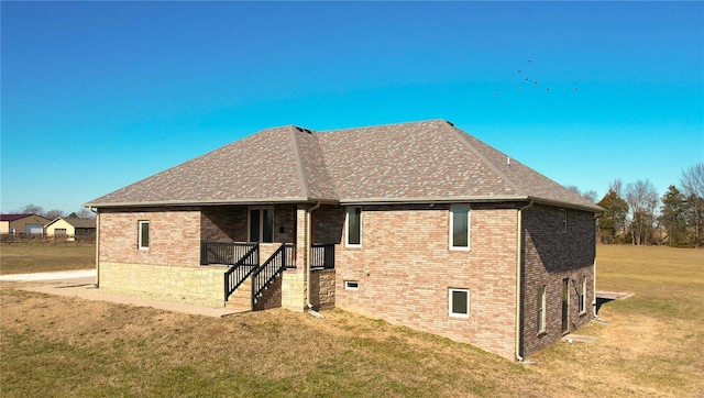 back of house with a shingled roof, brick siding, and a yard