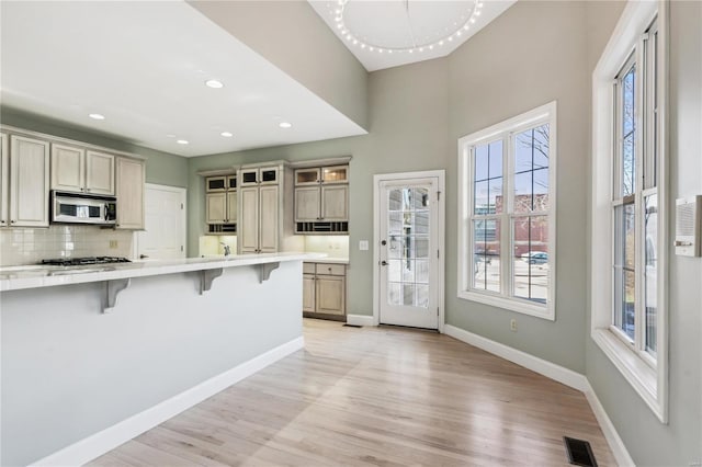 kitchen with cream cabinets, light hardwood / wood-style floors, a kitchen bar, decorative backsplash, and kitchen peninsula