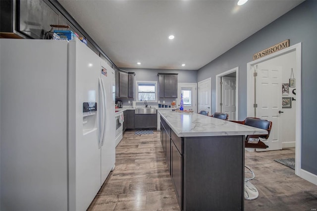 kitchen featuring dark brown cabinetry, sink, a center island, a kitchen breakfast bar, and white refrigerator with ice dispenser