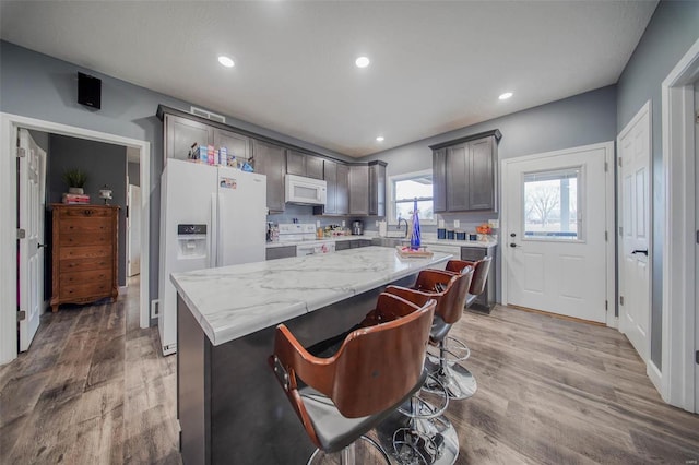 kitchen featuring a breakfast bar area, light wood-type flooring, a kitchen island, white appliances, and light stone countertops