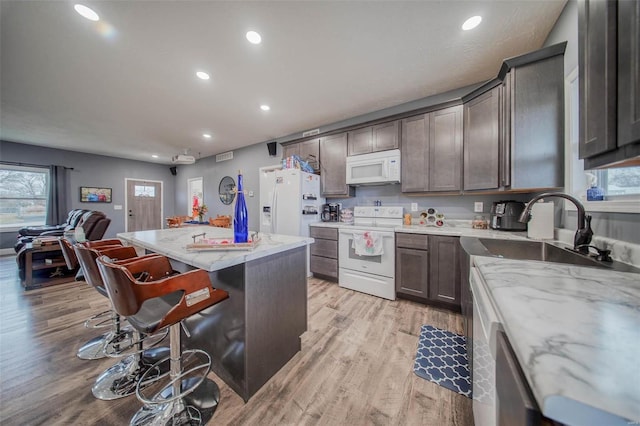 kitchen featuring a kitchen island, a breakfast bar, light stone countertops, white appliances, and light hardwood / wood-style flooring