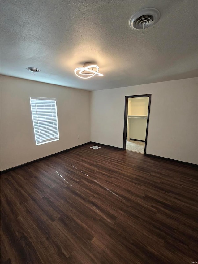 spare room featuring a textured ceiling and dark hardwood / wood-style flooring