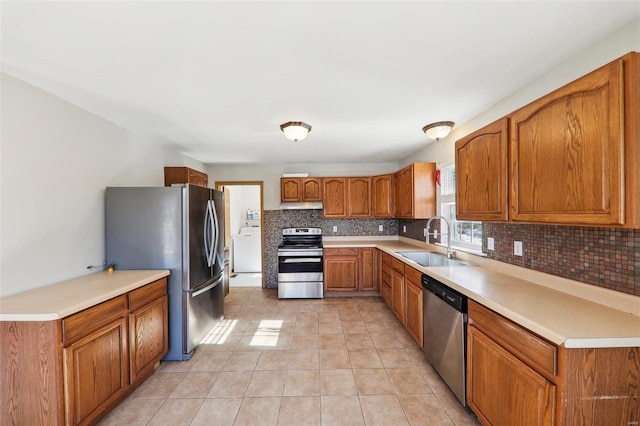 kitchen with washer / dryer, sink, tasteful backsplash, light tile patterned floors, and stainless steel appliances