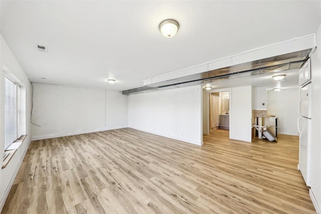 basement with light hardwood / wood-style floors and white fridge