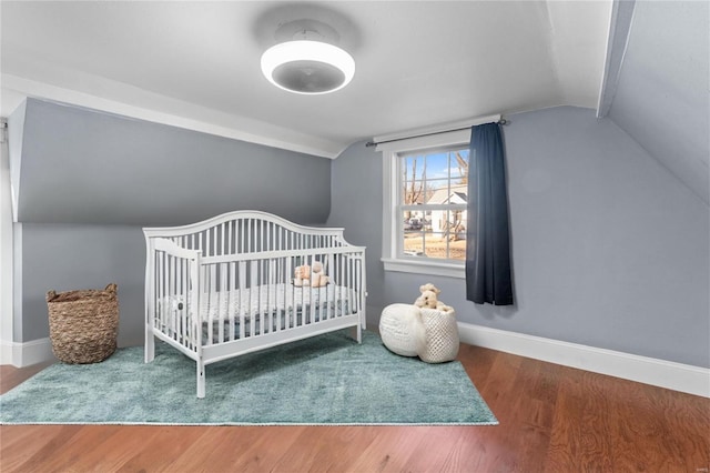 bedroom featuring lofted ceiling, hardwood / wood-style flooring, and a crib