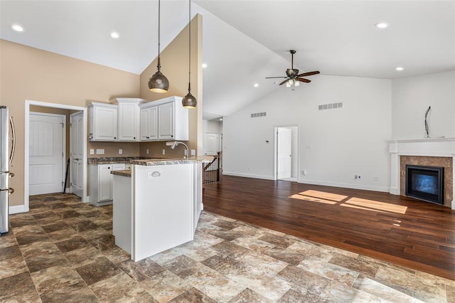 kitchen with a tile fireplace, white cabinets, pendant lighting, ceiling fan, and stainless steel fridge