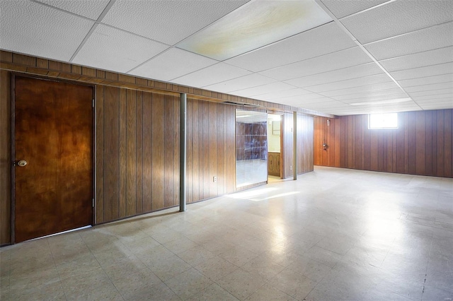 basement featuring wood walls and a drop ceiling