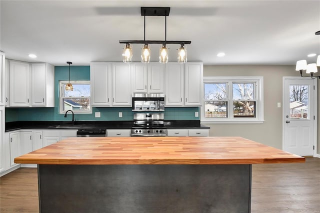 kitchen featuring butcher block countertops, white cabinetry, decorative light fixtures, a center island, and appliances with stainless steel finishes