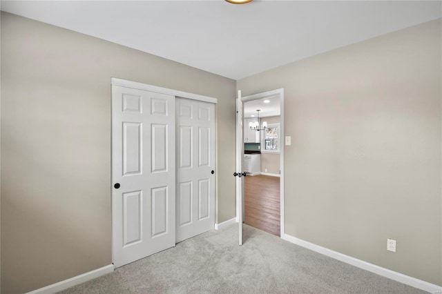 unfurnished bedroom featuring light colored carpet, an inviting chandelier, and a closet