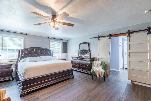 bedroom featuring ceiling fan, a textured ceiling, dark hardwood / wood-style flooring, and a barn door