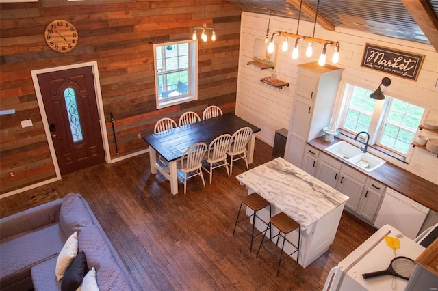 kitchen featuring decorative light fixtures, sink, wooden walls, white cabinetry, and beamed ceiling