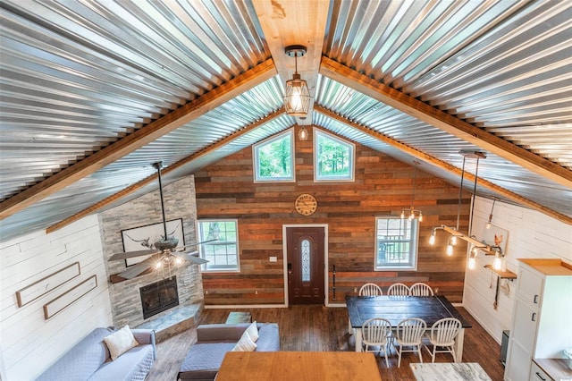 living room featuring ceiling fan, dark hardwood / wood-style floors, wood walls, vaulted ceiling with beams, and a stone fireplace