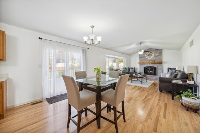 dining room featuring light hardwood / wood-style floors, a brick fireplace, lofted ceiling, and ceiling fan with notable chandelier