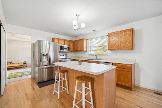 kitchen with a center island, appliances with stainless steel finishes, hanging light fixtures, a kitchen breakfast bar, and light wood-type flooring