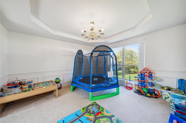 playroom featuring carpet floors, a tray ceiling, and an inviting chandelier