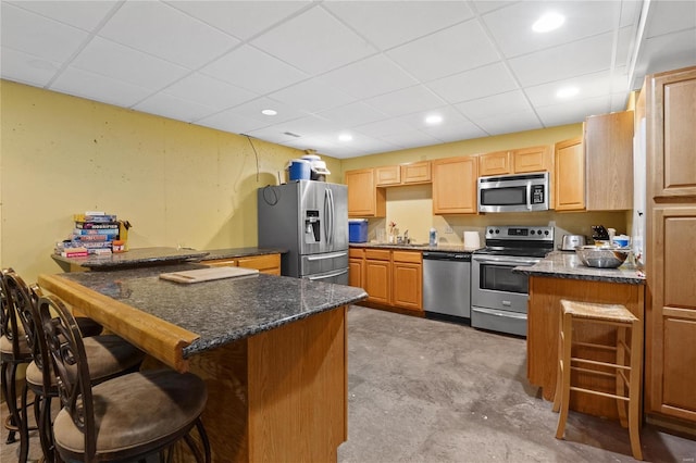 kitchen with dark stone counters, a kitchen breakfast bar, kitchen peninsula, stainless steel appliances, and a drop ceiling