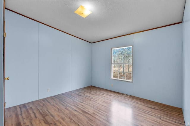 spare room featuring ornamental molding, light hardwood / wood-style floors, and a textured ceiling