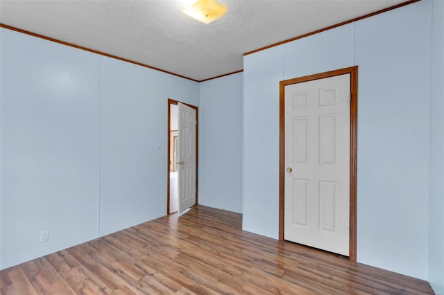 unfurnished room featuring crown molding, a textured ceiling, and light wood-type flooring