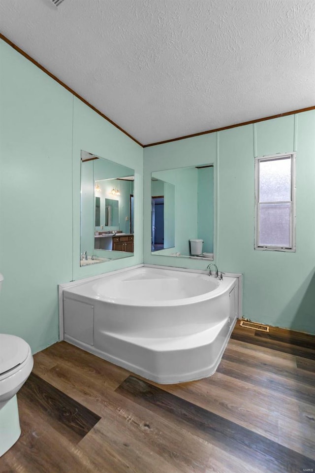 bathroom featuring hardwood / wood-style flooring, a tub to relax in, toilet, and a textured ceiling