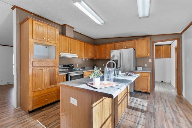 kitchen featuring lofted ceiling, ornamental molding, a kitchen island with sink, stainless steel appliances, and light hardwood / wood-style flooring