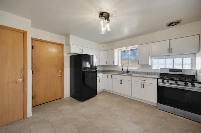 kitchen featuring black refrigerator, white cabinetry, sink, light stone countertops, and stainless steel gas range