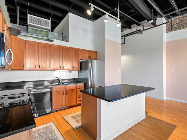 kitchen featuring appliances with stainless steel finishes, a towering ceiling, rail lighting, sink, and light hardwood / wood-style flooring