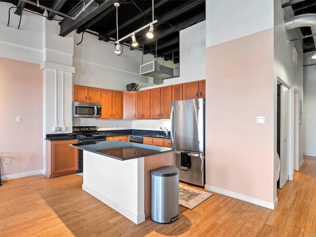 kitchen featuring rail lighting, a towering ceiling, light hardwood / wood-style floors, and black appliances