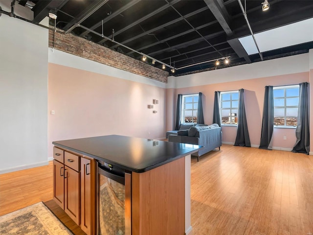 kitchen featuring a high ceiling, track lighting, light hardwood / wood-style floors, a kitchen island, and beverage cooler