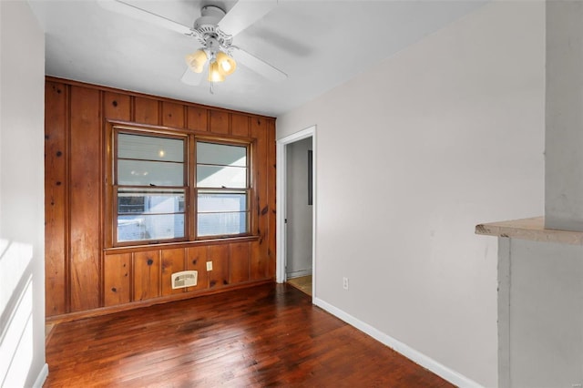 empty room with ceiling fan, wood walls, and dark hardwood / wood-style flooring