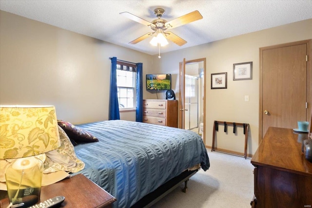 bedroom with ceiling fan, ensuite bath, light colored carpet, and a textured ceiling