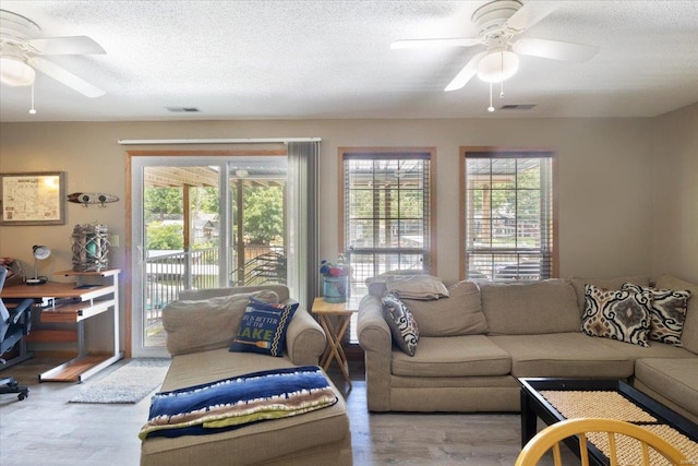 living room featuring hardwood / wood-style flooring, ceiling fan, and a textured ceiling