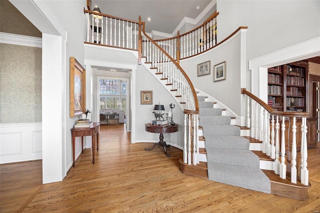 entryway with ornamental molding, light hardwood / wood-style flooring, and a high ceiling