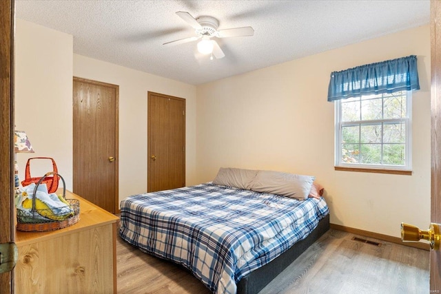 bedroom featuring hardwood / wood-style flooring, two closets, a textured ceiling, and ceiling fan