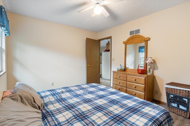 bedroom featuring white refrigerator, hardwood / wood-style flooring, a textured ceiling, and ceiling fan