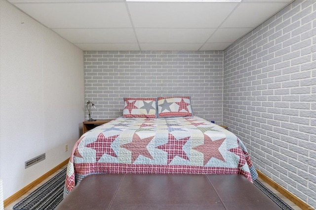 bedroom with brick wall and a paneled ceiling