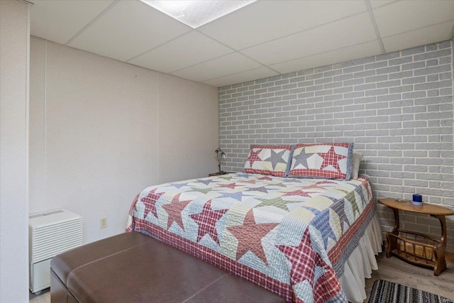 bedroom featuring hardwood / wood-style floors, a paneled ceiling, and brick wall