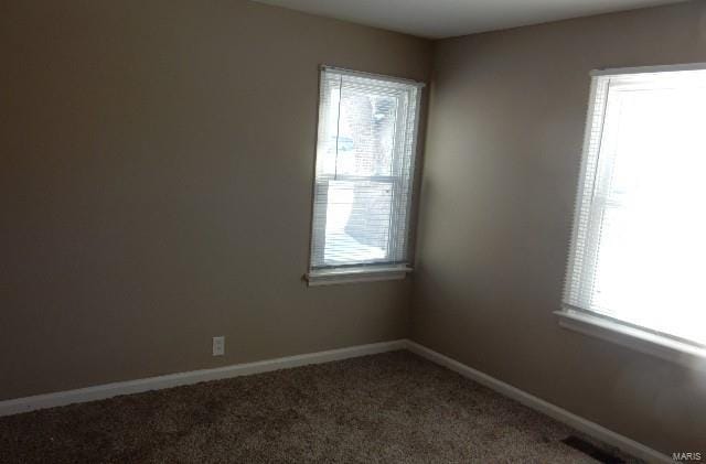 unfurnished room with a healthy amount of sunlight, dark carpet, visible vents, and baseboards