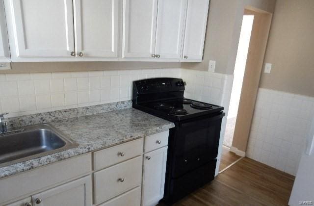 kitchen with dark wood-type flooring, black range with electric stovetop, light stone countertops, white cabinetry, and a sink