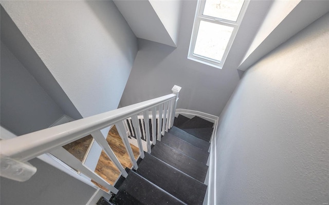 stairway with a textured wall, wood finished floors, and baseboards