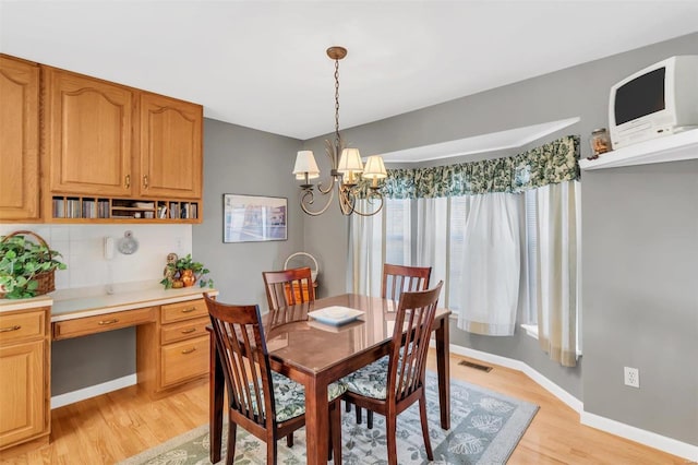 dining space featuring light wood-type flooring, a chandelier, and built in desk